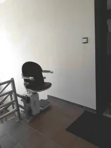 Αναβατόριο καρέκλα σκάλας με σκούρο κάθισμα, παρκαρισμένο στο πλατύσκαλο στην κορυφή της σκάλας.