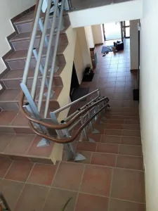 Άποψη από ψηλά μιας σκάλας πολλαπλών επιπέδων με καφέ πλακάκια, όπου φαίνεται η εγκατεστημένη ράγα ενός αναβατορίου σκάλας να ακολουθεί τις στροφές.