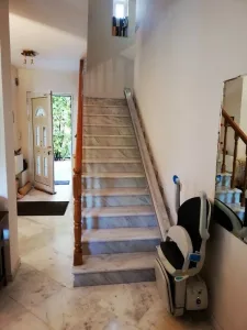 Αναβατόριο καρέκλα σκάλας παρκαρισμένο στο κάτω μέρος της σκάλας, δίπλα στην είσοδο του σπιτιού.