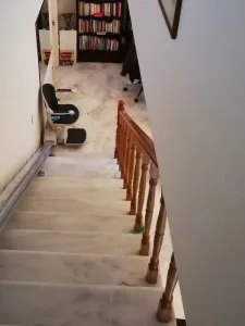 Άποψη από την κορυφή μιας μαρμάρινης σκάλας προς τα κάτω, όπου φαίνεται ένα αναβατόριο σκάλας παρκαρισμένο στο ισόγειο.