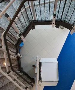 Κάτοψη πλατφόρμας αναβατορίου για αμαξίδιο σε καμπυλωτή σκάλα με μεταλλικά κάγκελα.