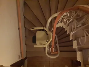 Κάτοψη ενός αναβατορίου καρέκλας καθώς κινείται σε μια καμπυλωτή, ξύλινη σκάλα με περίτεχνα κάγκελα.