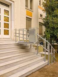 Αναβατήρας σκάλας για αναπηρικά αμαξίδια σε εξωτερικό χώρο με μαρμάρινα σκαλιά και κτίριο στο φόντο.